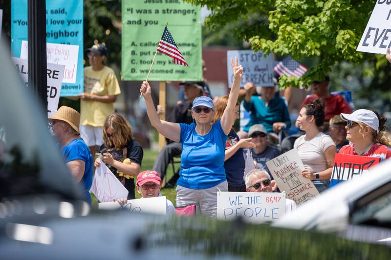 Protester waves American flag and holds up peace sign at the “No Kings” protest as cars drive past on north Main Street on Saturday, June 14, 2025 at Rotary Park in Princeton.