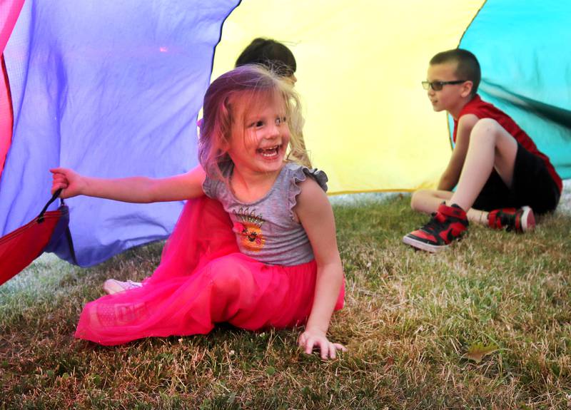 Kids play with a parachute Friday, June 14, 2024, at Hopkins Park. The park district was hosting a Dedication Celebration event at the park for the grand opening of the new playground and racquet courts.
