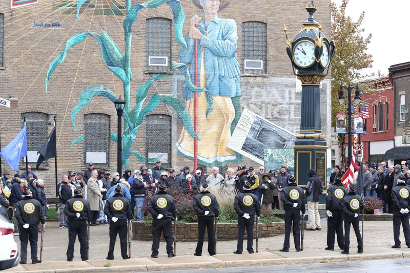 A crowd of about 100 people gather at Memorial Park to listen to speakers as the DeKalb American Legion Post 66 Honor Guard stands watch Thursday, Nov. 11, 2021, during a Veterans Day and Soldiers' and Sailors' Memorial Clock rededication ceremony in downtown DeKalb.