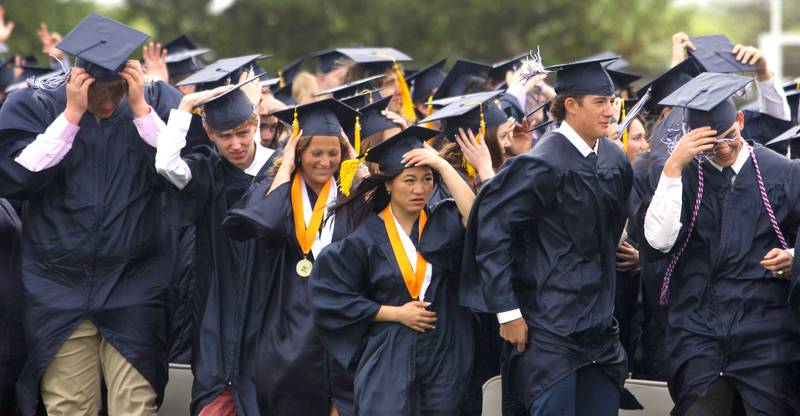 Members of the Class of 2025 face a stiff wind as they search for loved ones in the crowd during graduation at Cary-Grove High School in Cary on Saturday, May 17, 2025.