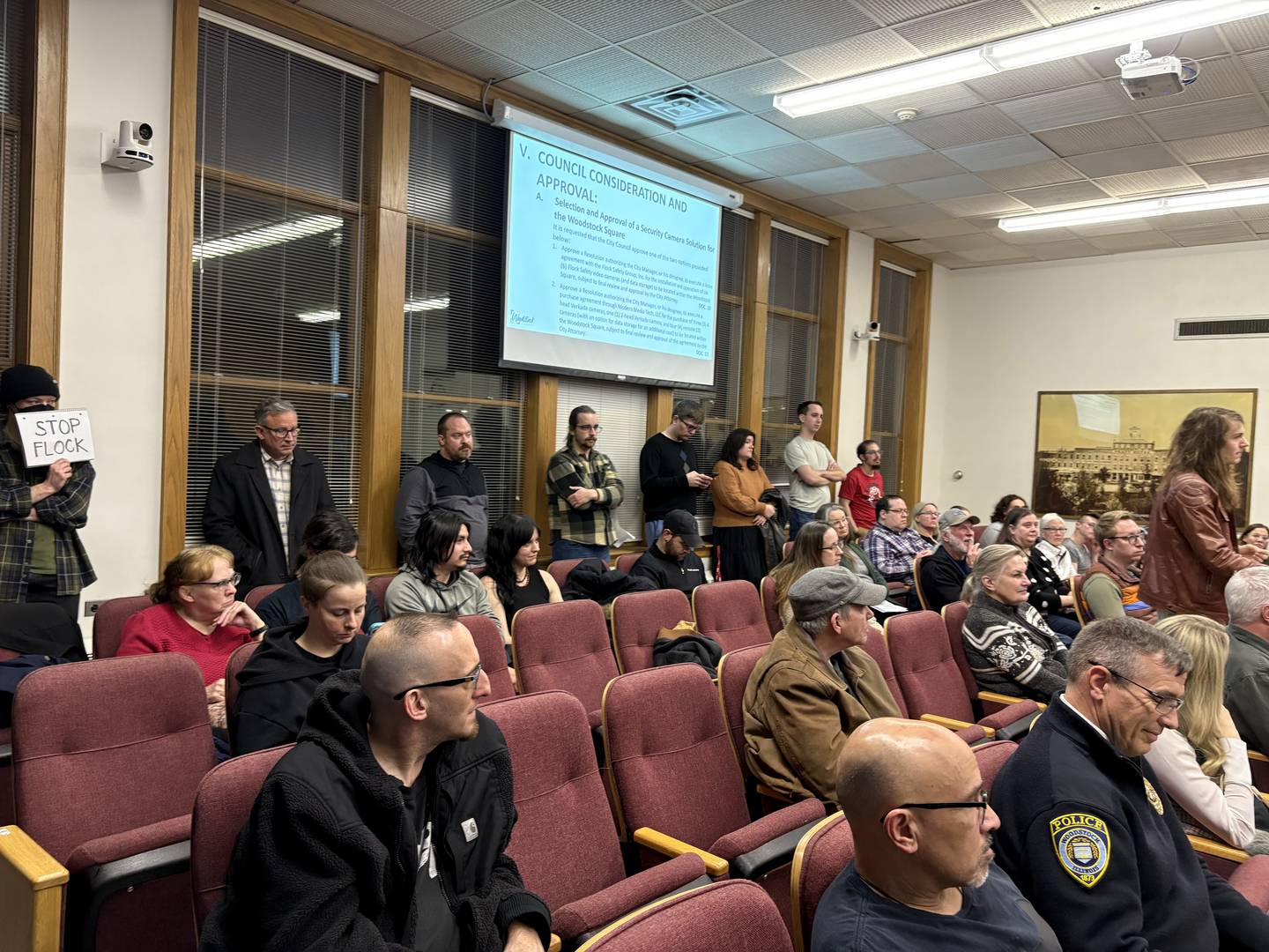 An audience member at far left holds up a "Stop Flock" sign while another member of the public addresses the Woodstock City Council on Feb. 3, 2026, before the Council voted in favor of installing Flock cameras on Woodstock Square.