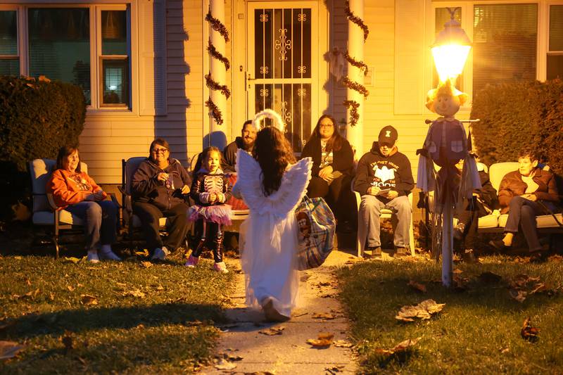 A child dressed as an angel approaches the Bradley home of Jean Tanner, left, as her neighbor, Madonna Bertrand, second from left, gather with friends and family to greet trick-or-treaters on Friday, Oct. 31, 2025.