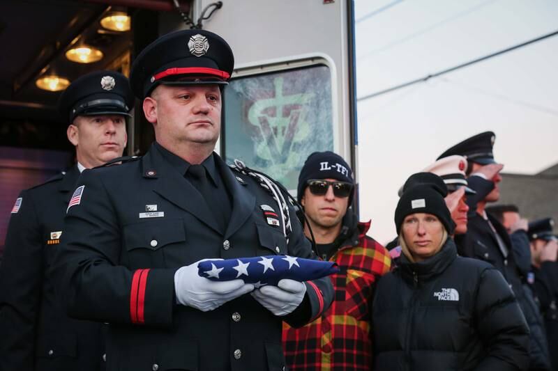 West Chicago firefighter paramedic Todd Baseggio holds the flag for K-9 Irie, a search-and-rescue dog who died Sunday, Dec. 4, 2022, at her home in Johnsburg after her early medical retirement from the Lincolnshire-Riverwoods Fire Protection District.