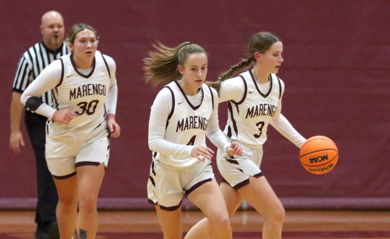 Marengo’s Maggie Hanson, right, moves the ball as Katie Hanson, center, and Macy Noe, left, head downcourt against Woodstock North in varsity girls basketball on Tuesday, Dec. 2, 2025, at Marengo High School in Marengo.