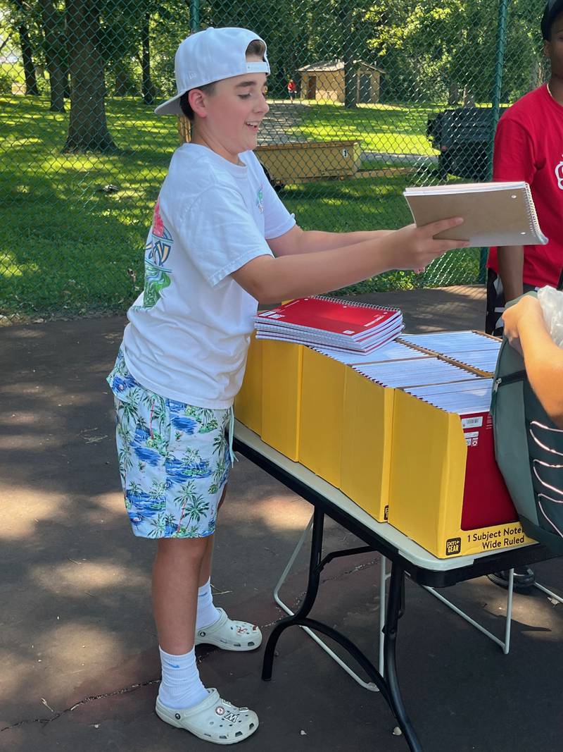 Eighth-grader Owen Staabe hands out new notebooks to fellow students during the Joliet Park District's back-to-school event at Nowell Park. on Saturday, Aug. 9, 2025.