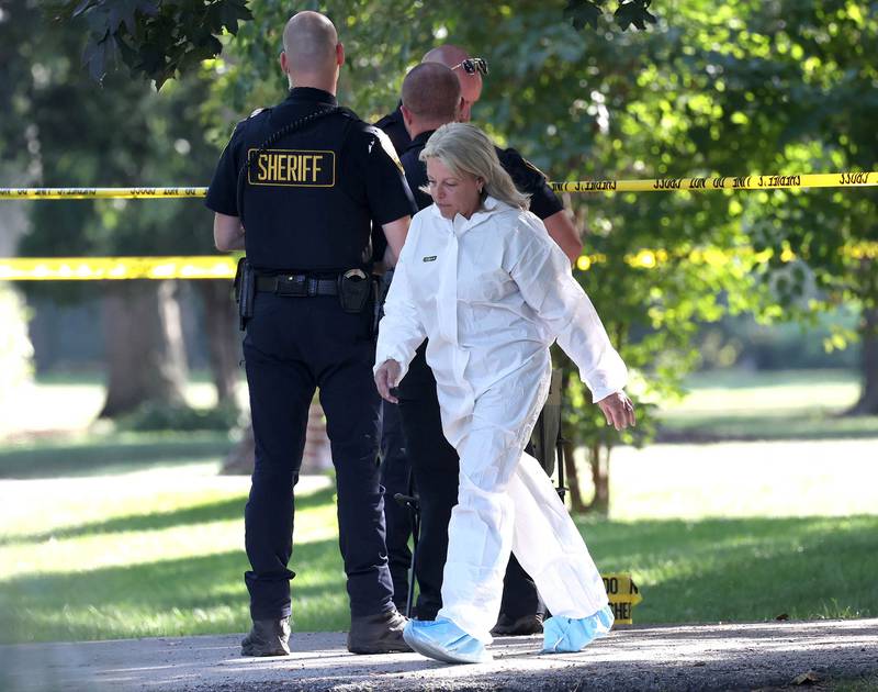 A DeKalb County sheriff’s deputy lifts the crime scene tape for an investigator in a protective suit Tuesday, Sept. 30, 2025, in front of a house in the 1300 block of Oakland Drive in Sycamore where two people were found dead Tuesday morning.