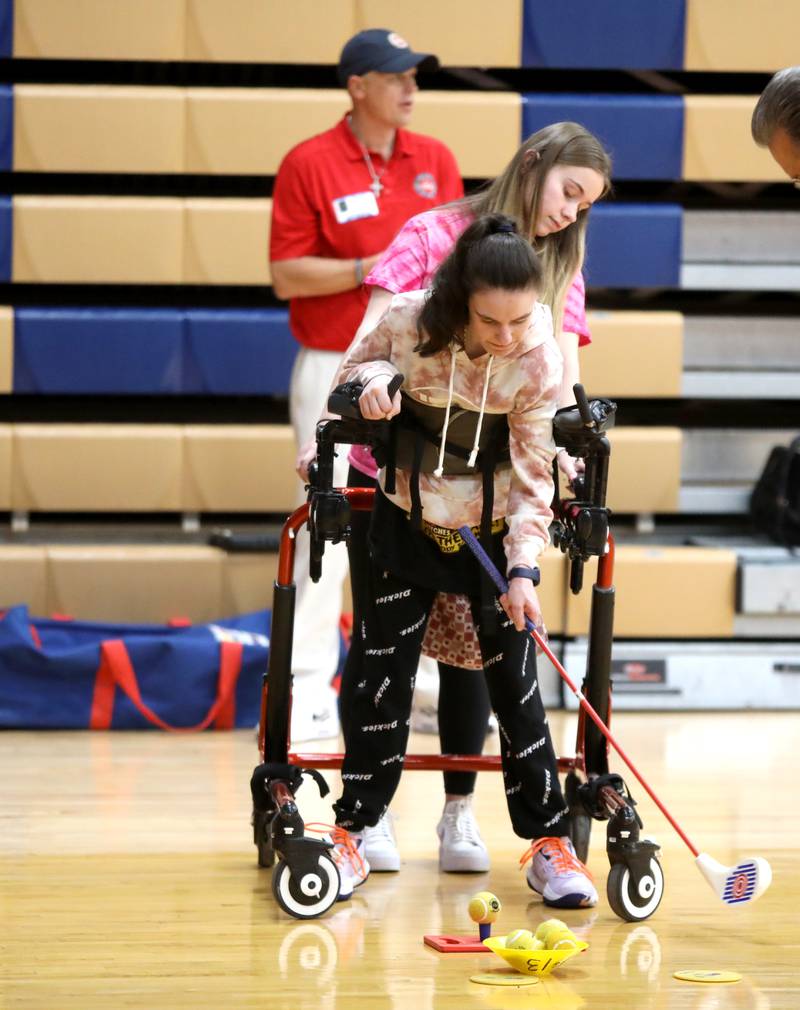 Oswego High School student Grace Atwood, with the help of classmate Mila Knoblock, tees up her golf shot during their physical education class at Oswego High School on Monday, March 4, 2024. The class was part of a six-week program collaboration with the U.S. Adaptive Golf Alliance.