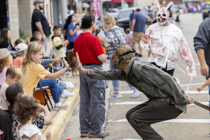 Lia Romero, 8, gets a high five from Jason, a character of “Hells Horror,” a newly formed haunted house in Rock Falls Saturday, Sept. 16, 2023 during the Sauk Valley Fiesta Days parade.