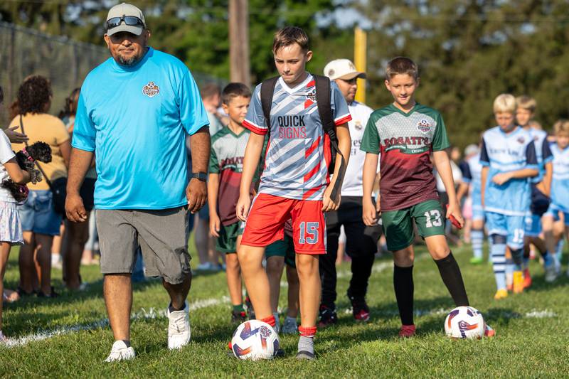 (from left) Coach Salvador walks with Lucas Vanwiggeren at the opening day ceremony of youth soccer on Saturday, Aug 16, 2025, at Peck Park in Ottawa.