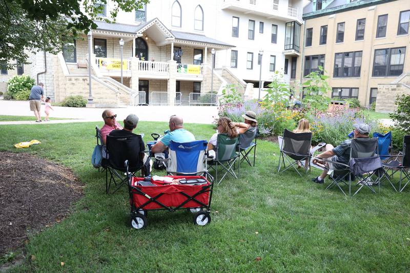 A group finds shade on the lawn as Anne Hatfield-Martin performs on the balcony of USF Motherhouse. The Upper Bluff Historic District hosted Porch & Park Music Fest featuring a variety of musical artist at five different locations. Saturday, July 30, 2022 in Joliet.