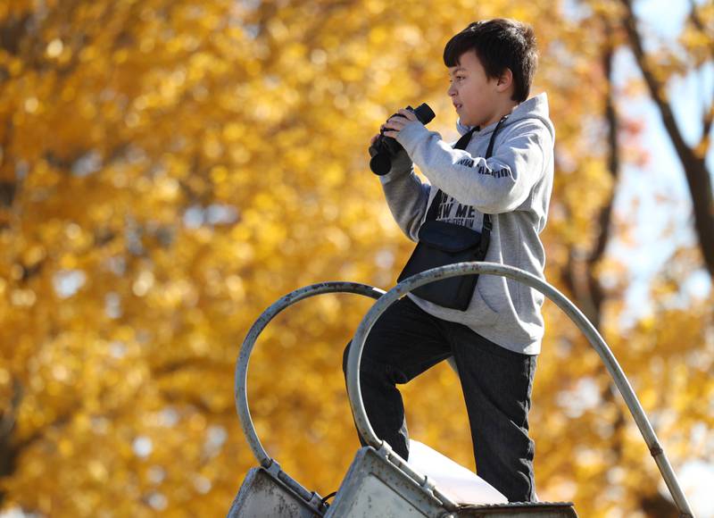 Southeast Elementary School third grader Finn Acevedo looks a local farms in the area with binoculars from atop a slide Tuesday, Nov. 4, 2025, as he and his classmates learn about school in the 19th century during a visit to North Grove School, a one-room schoolhouse from 1878 in Sycamore.