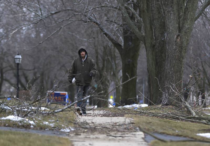 A pedestrian navigates downed tree branches as he walks along Dole Avenue near Ash Street in Crystal Lake on Thursday, Feb. 23, 2023, as county residents recover from a winter storm that knocked down trees and created power outages throughout McHenry County.