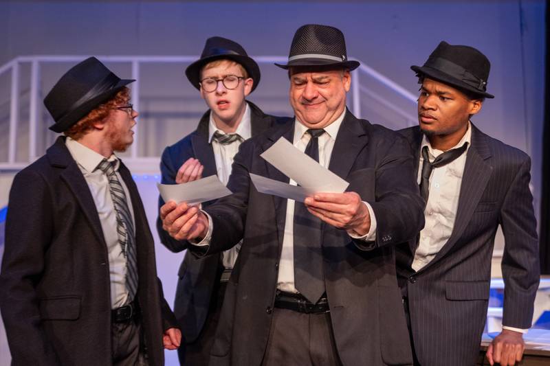 (left to right) “Cod” (Played by Forrest Boes), “Dollar” (Played by Cole Roark), “Jeff Sudakov” (Played by Carl Hanratty) and “Branton” (Played by Jeremiah Noar) gather around fake checks on Monday, March 24, 2025 at River Valley Players Theatre in Henry.