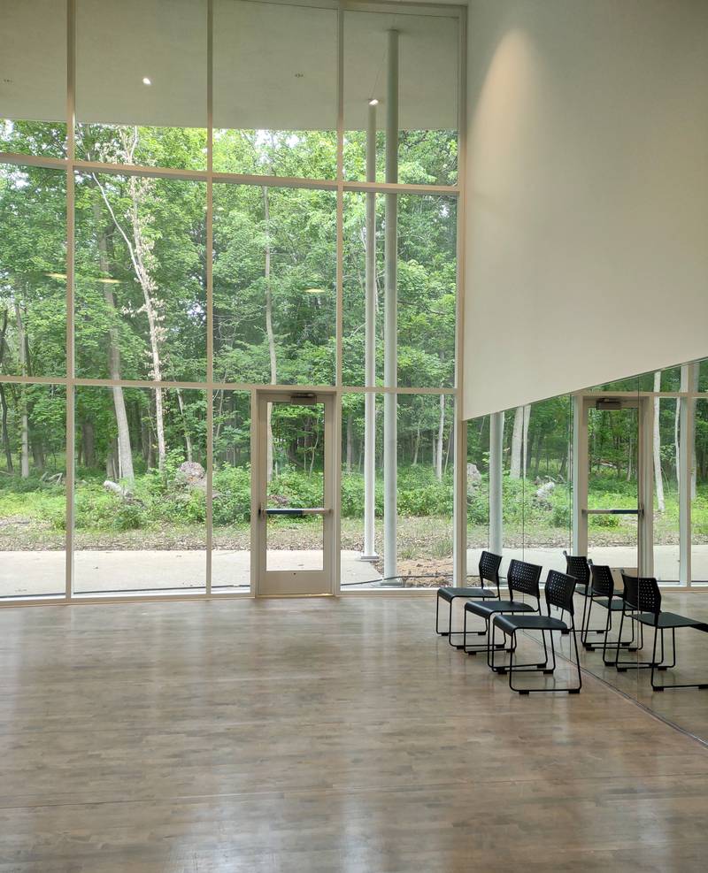 Floor-to-ceiling windows fill a studio space with natural light and views of nature inside the Health and Wellness Building at Nell's Woodland in Ottawa. The Health and Wellness Building includes spaces for wellness classes such as yoga, as well as meeting spaces, a kitchenette and special function rooms.