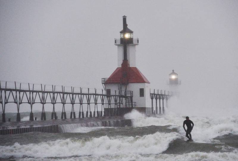 A surfer rides through blowing snow as Lake Michigan waves crash into the St. Joseph Inner and Outer Lighthouses Wednesday, Nov. 26, 2025, in St. Joseph, Mich. (Don Campbell/The Herald-Palladium via AP)