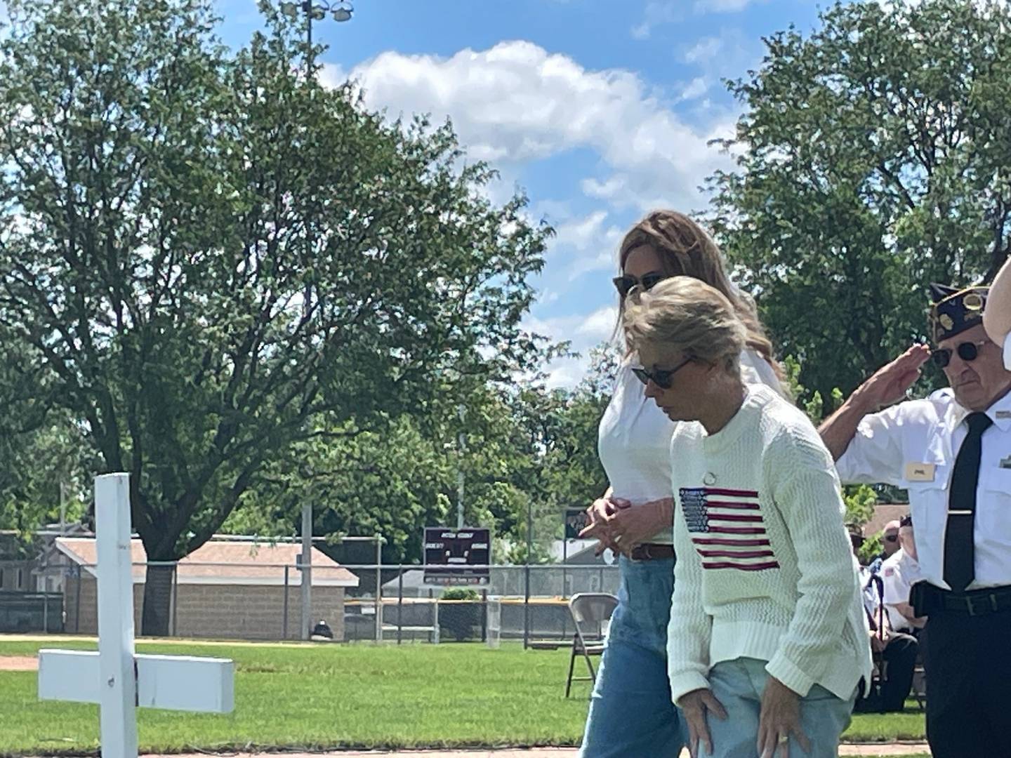 Deb Dahl (foreground), widow of state Sen. Gary Dahl, rises after placing a ceremonial wreath before a cross during Memorial Day services Monday, May 27, 2024, in Washington Park, Peru. To Deb's right is Gary Dahl's daughter Kim. Phil Valle, chaplain of the Peru Veterans Memorial Group, salutes at the wreath placement. Peru services were held in honor of Gary Dahl for all the work he had done on behalf of veterans in the Illinois Valley.