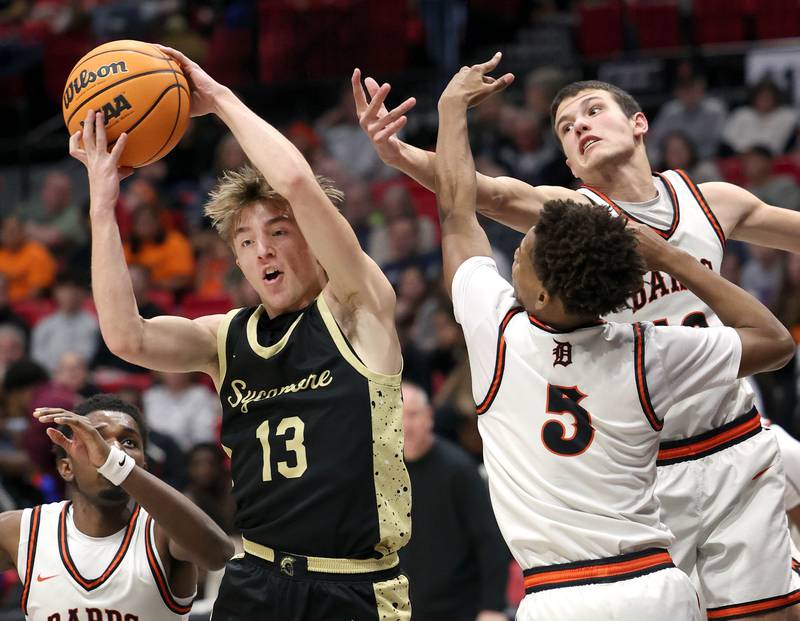 Sycamore's Xander Lewis grabs a rebound between DeKalb's Myles Newman (left) DeKalb's Jack Rosenow and DeKalb's Bryan Miller Friday, Jan. 30, 2026, during the FNBO Challenge at the Convocation Center at Northern Illinois University in DeKalb.