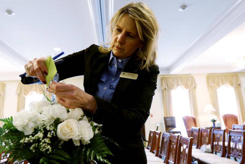 Davenport Family Funeral Home attendant Pam Ross attaches a card to a flower arrangement before a public visitation for Andrew "AJ" Freund on Friday in Crystal Lake.