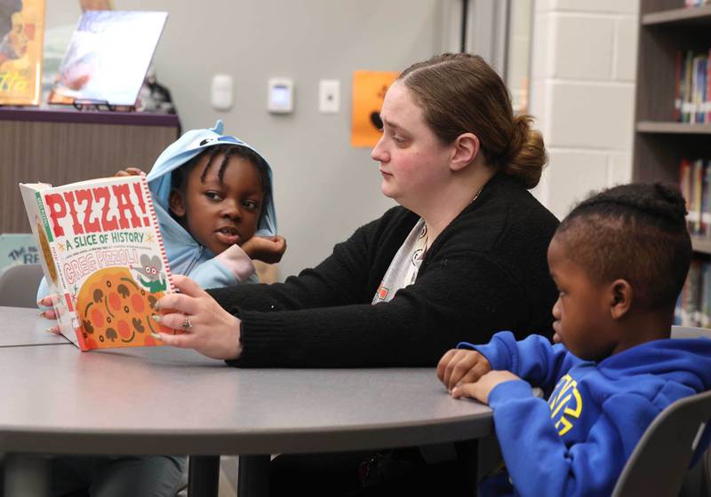 Mitchell Elementary School first grade teacher Cassandra Sprankle reads a book to Savannah Holden and Bryson Williams Thursday, March 19, 2026, in the library at the school in DeKalb.