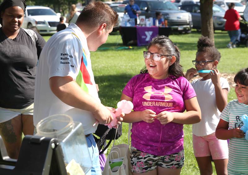 Jonathan Sass, from FBI Entertainment, talks to Mia Marquez, 9, from Genoa, as he makes her a balloon animal during the Family Fun Fest Wednesday, July 17, 2024, at Hopkins Park in DeKalb.