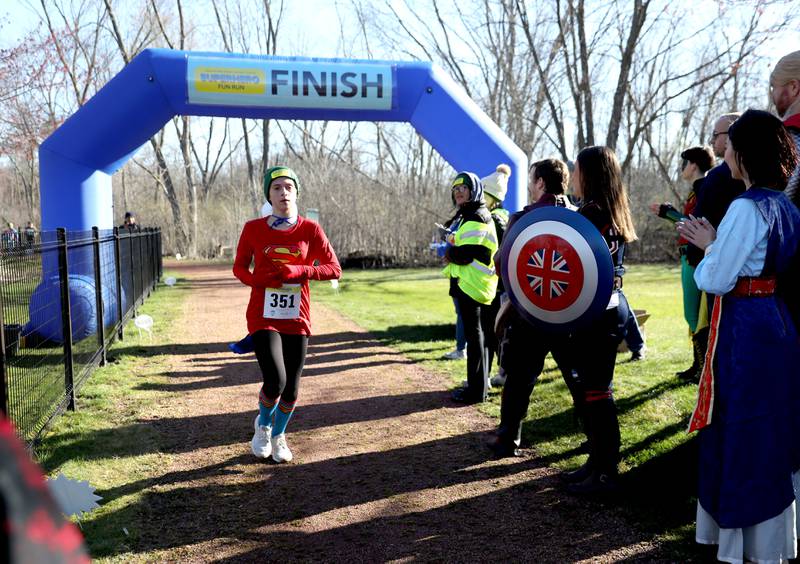 Mackenzie Pelhank, 14, of Wheaton is greeted by Super Heroes at the finish of the Wheaton Park District’s Superhero 3K Fun Run at the Sensory Garden Playground in Lisle on Saturday, April 6, 2024.