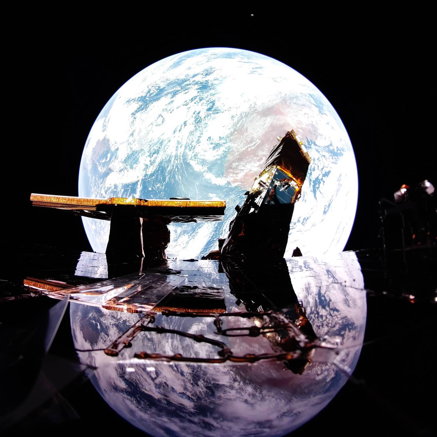 Image of Earth reflecting off a solar panel with the Moon (top, in distance) on the horizon, taken from aboard the Blue Ghost lunar lander, on Feb. 12, 2025.