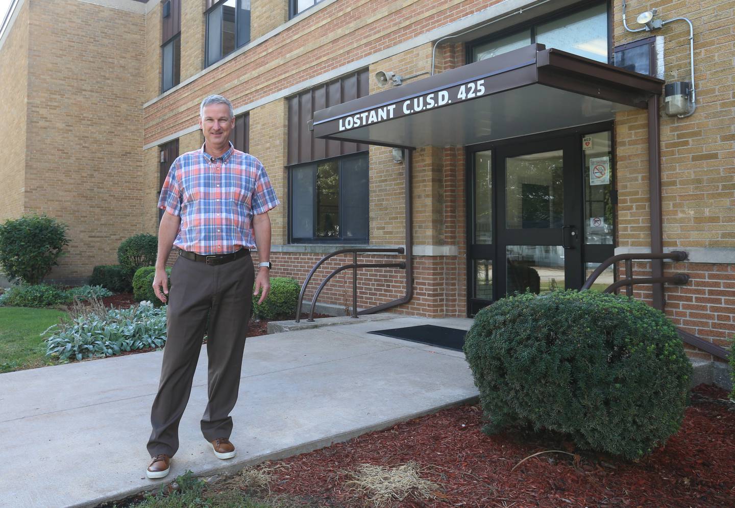 Lostant Grade School superintendent Bob Ketcham poses next to the main entrance on Tuesday, Sept. 12, 2023. Lostant Grade School now shares a superintendent with Tonica Grade School. The two districts are not merging; but a shortage of educators, including administrators, prompted the districts to hire Ketcham in a rare (but not unprecedented) dual role.