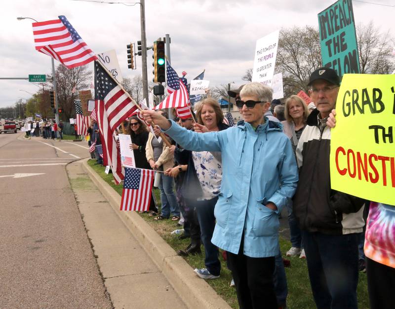 Protesters wave flags and hold signs along Sycamore Road Saturday, April 19, 2025, during a “No Kings” rally and march starting at Hopkins Park in DeKalb. The group was protesting what they’ve argued is the unlawful and harmful federal policies of President Donald Trump and his administration.