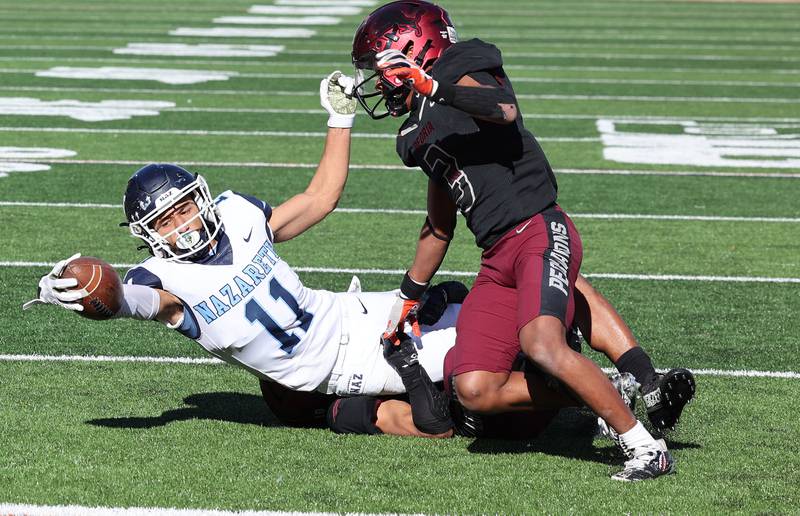 Nazareth's James Penley stretches for the goal line while being brought down by two Peoria defenders during their IHSA Class 5A state championship game Saturday, Nov. 26, 2022, in Memorial Stadium at the University of Illinois in Champaign.