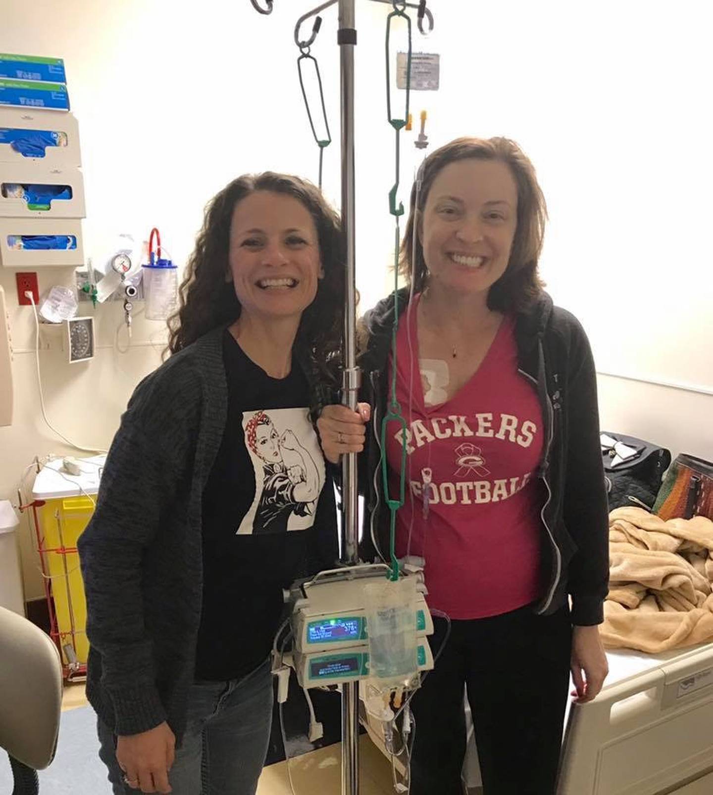 In 2017, Jessica Catlin (left) stands with her friend Hilary Moore during one of Catlin's eight chemotherapy sessions for colorectal cancer.