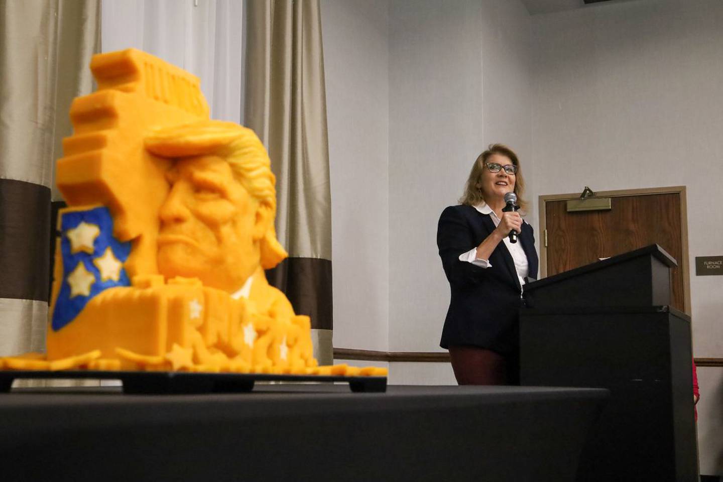 Illinois GOP Chair Kathy Salvi speaks to the Illinois delegation to the 2024 Republican National Convention at a breakfast meeting at a suburban Milwaukee hotel alongside a cheese carving of President Donald Trump and the state of Illinois.