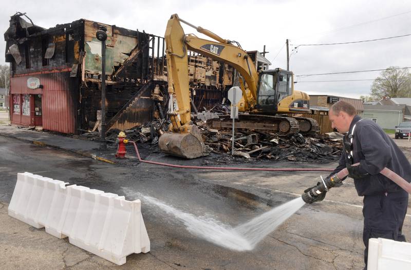 Mt. Morris Fire Captain Mark Lewis washes away soot from Wesley Avenue in downtown Mt. Morris on Wednesday, April 17, 2024 following Tuesday's fire that destroyed two downtown buildings. The buildings were adjoined and did not have a fire wall separating them. Sharky's Sports Bar remained standing on Wednesday. An excavator stands where the other bulding was located. Portions of that building were removed as a safety precaution. An official cause of the fire has yet to be determined.