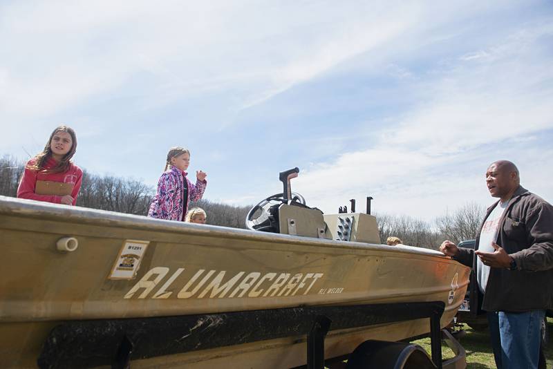 Fifth graders Chloe Murphy (left) and Olivia Fullington listen as volunteer Neil Hightower discusses the boat used at the hatchery. The entire process of gathering, harvesting, growing and releasing the fish are all handled by volunteers.