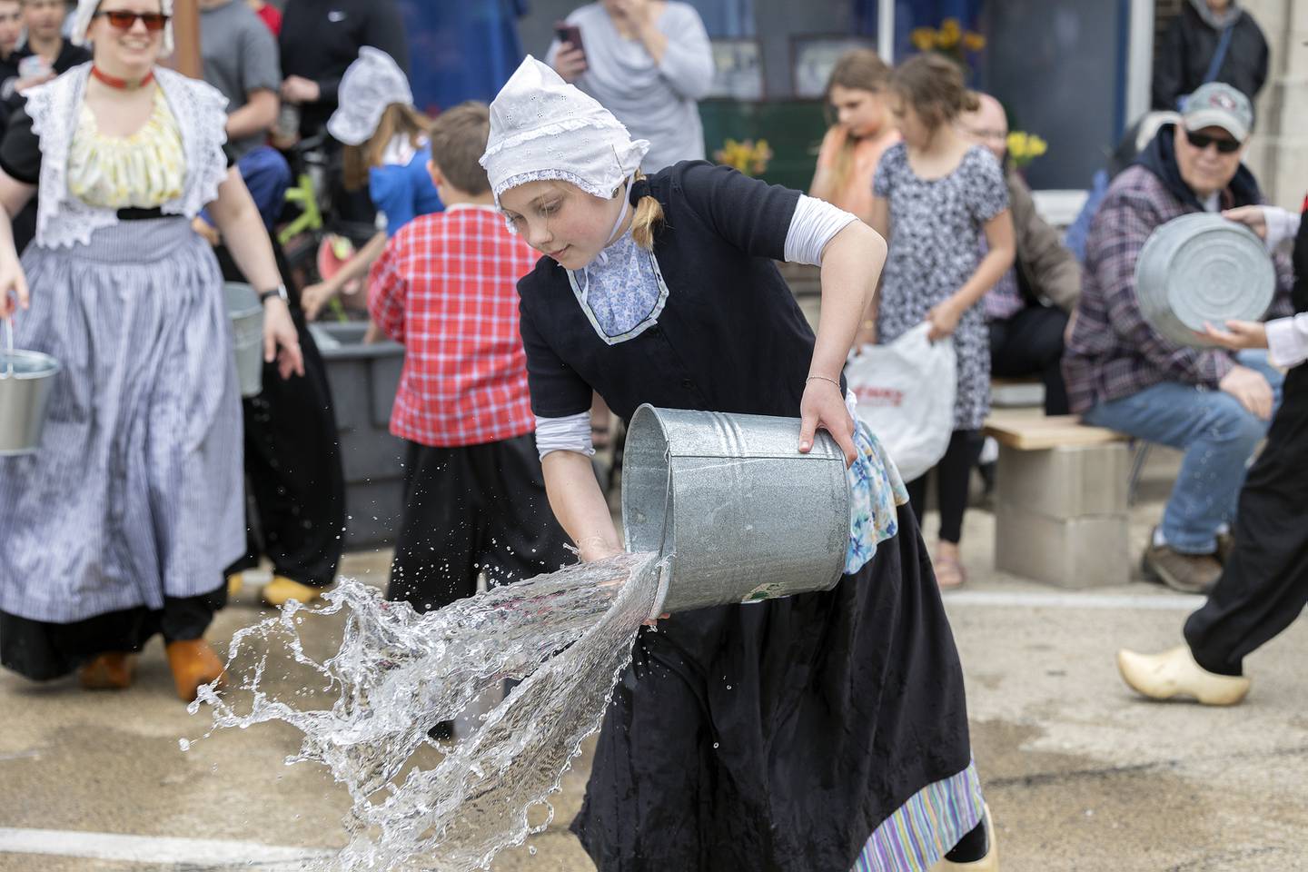 A youngster tosses a bucket of water onto the streets of Fulton Saturday, May 3, 2025, as the traditional cleaning of the parade route takes place during Fulton’s Dutch Days.