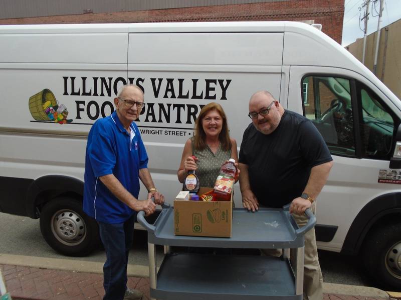 Mary Jo Credi (center), executive director of the Illinois Valley Food Pantry,  shows one of the meal packs ready for distribution to Sam Sankovich (right), Oglesby Elks Lodge Exalted Ruler and Grant Coordinator Ken Ficek (left). Oglesby Elks has supported the IV Food Pantry with a $2,500 monetary donation and helped pack and distribute food during the holidays.