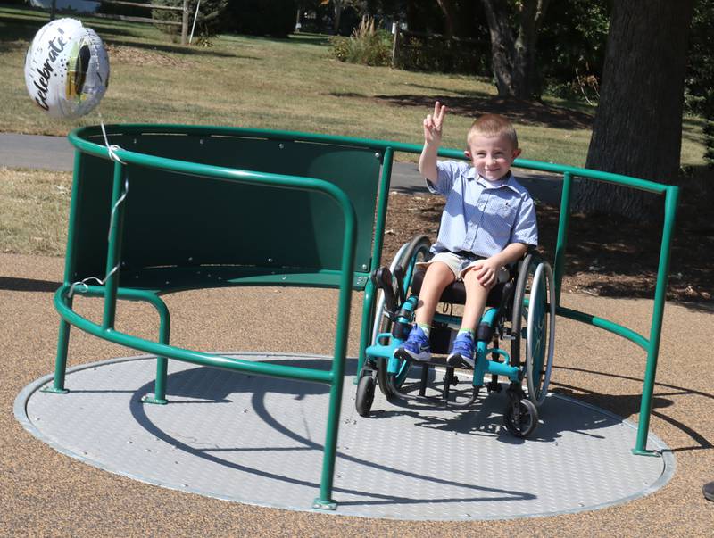 James Graham 7, of Princeton, holds a "piece" sign as he spins on the new in-ground merry-go-round  during a new playground dedication on Monday, Sept. 15, 2025 at Zearing Park in Princeton. The 7,000 square-foot playground features sensory panels, in-ground merry-go-round with back support, slides, swings, health development and creative play. Half of the project was paid for by a OSLAD grant and the other half was purchased by the Princeton Park District. No tax dollars were used for the project.
