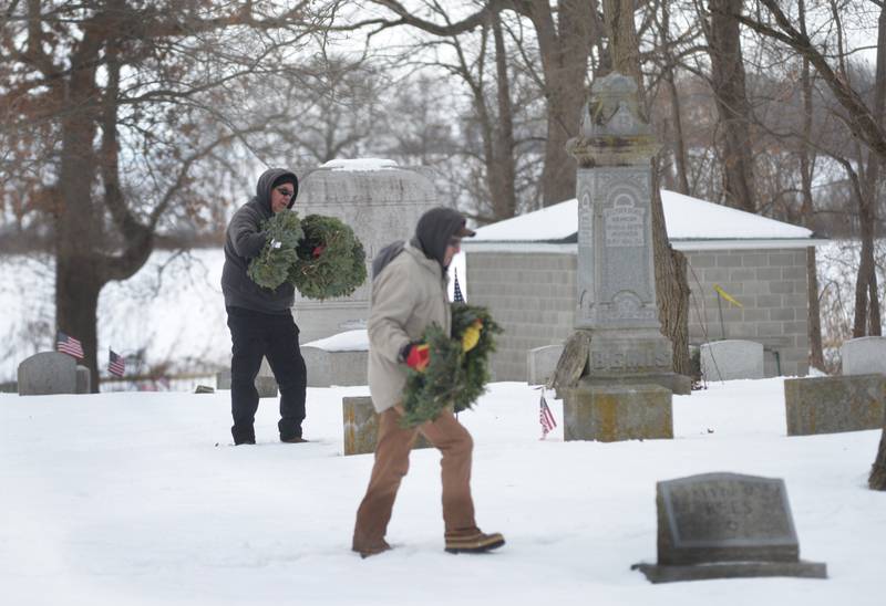 Two volunteers trudge through the snow to  lay wreaths on veterans' graves at the Daysville Cemetery during the Wreaths Across America program on Saturday, Dec. 13, 2025.