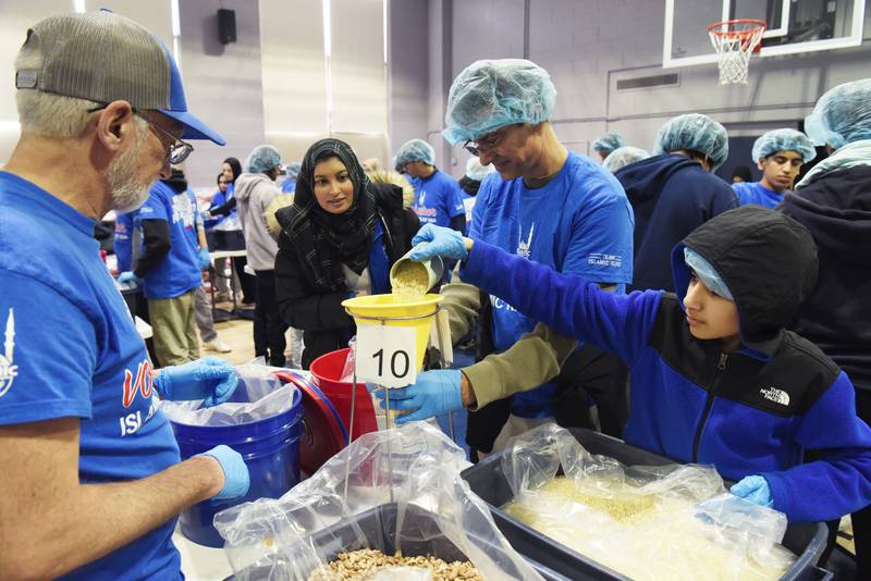 Adam Peer, 12, of Westmont, his dad, Nawshad, upper right, and Robert Erck of Darien, left, add ingredients to their first package as Wsmah Siddiqui instructs them during the Islamic Relief USA meal packing event at College Preparatory School of America on Saturday, March 9, 2024 in Lombard.