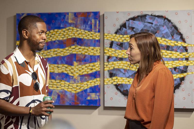 Sauk Valley College economics professor Jon Devereueawax and english professor Rachel Brunner converse in front of art works by art professor Glenn Bodish Wednesday, April 26, 2023. The college held an opening for a faculty and staff art show at in the school’s gallery. The show will run until Sept. 5.