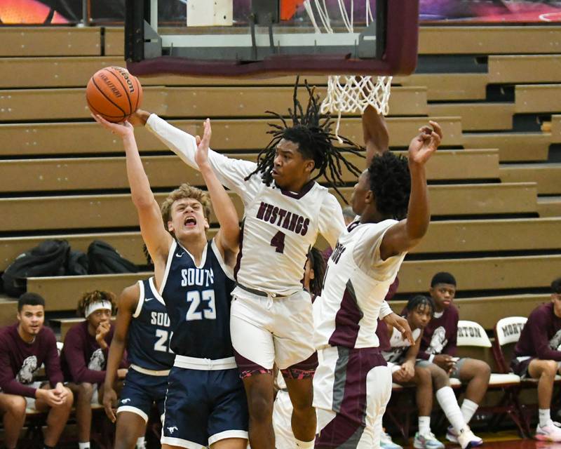 Morton East's Twon Jones (4) blocks the shot of Downers Grove South's Joe Grippo (23) with assistance of Morton East teammate Tyler Nichols (11) during the first quarter on Saturday Dec. 9, 2023, held at Morton East High School.