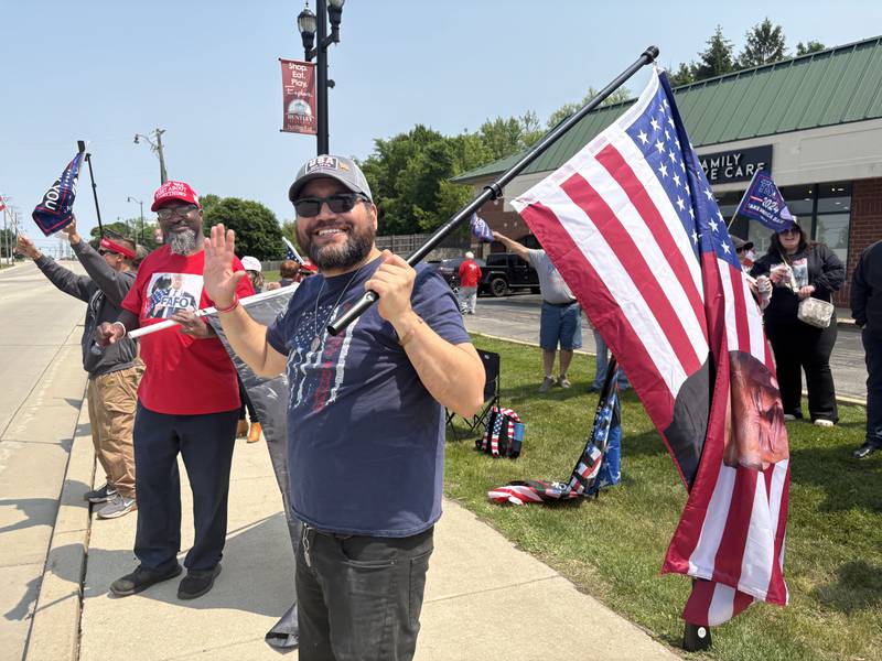 Angel Santana, right, waves to a car during a rally outside the Trump and Truth Store in Huntley.