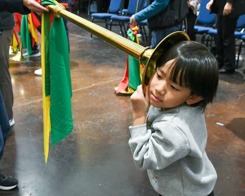 Othniel Tan,6, of Schaumburg puts his ear up to the bell of the long trumpet as community members get to try their hand at the instruments used during the performance from the students of Jhong Jheng Elementary School Suona and Drum Ensemble from Kinmen, Taiwan, on Saturday April 19, 2025, held at the Taiwanese American Chamber of Commerce building in Westmont.