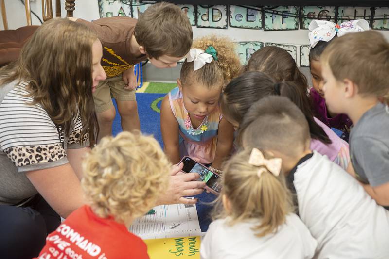 Students gather around teacher Janelle Dykstra’s phone to learn about cricket sounds during instruction Thursday.