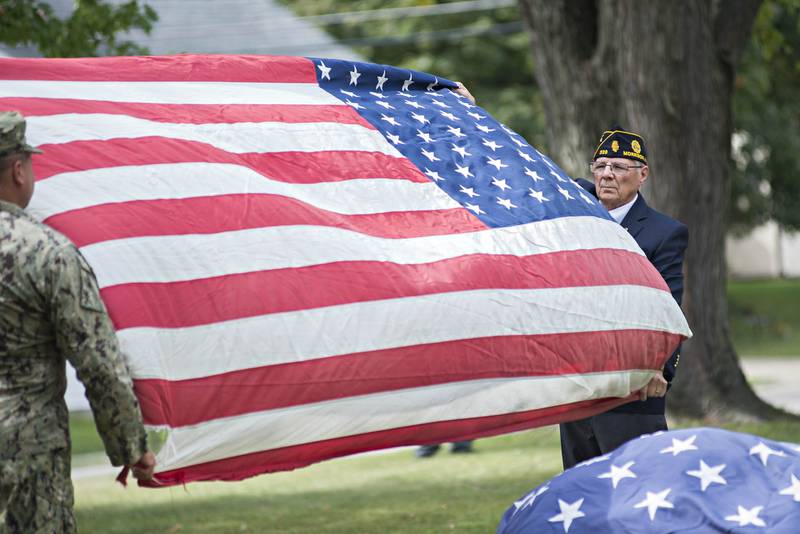 Morrison American Legion commander Larry Zuidema (right) and Dennis VanZuiden unfurls a flag that will be honorably burned after having served their duty. The legion retired 307 flags on Sunday.