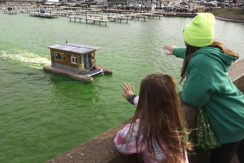 Morgan Dervis, 6, and Raina Lucas, 12, waver to a boater as the Fox River is dyed green during the ShamROCKS the Fox Festival in McHenry on Saturday, March 16, 2024.