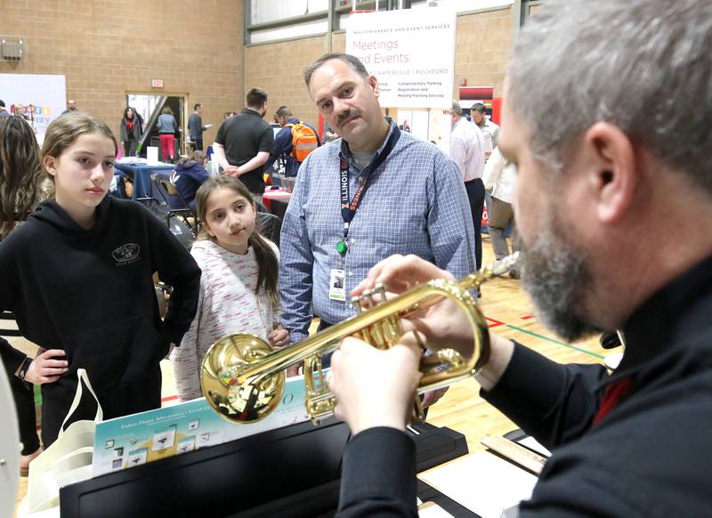 Ben Weaver, owner of the Music Connection in Sycamore, demonstrates the trumpet at his booth to Jose Hinojosa and his daughters Victoria, (left) 12, and Amelia, 9, during the DeKalb Chamber of Commerce’s Local Showcase and Job Fair Thursday, April 25, 2024, at the DeKalb Sports and Recreation Center.