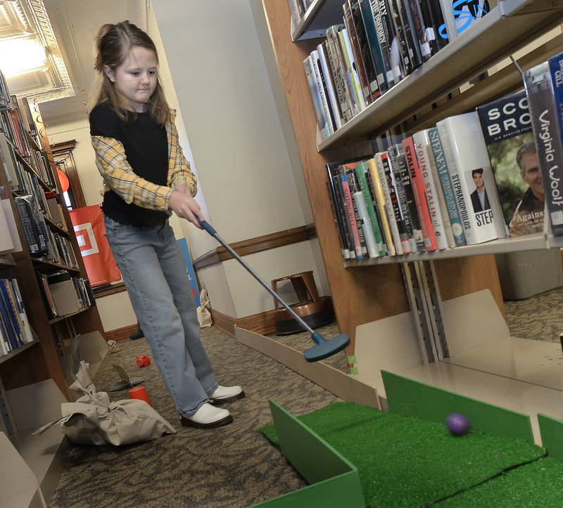 On a narrow hole surrounded by books, Zoey Mason tries to sink this putt  Saturday, Jan. 21, 2023, during the Streator Public Library’s inaugural mini-golf fundraising event. Each hole was sponsored by a local business.