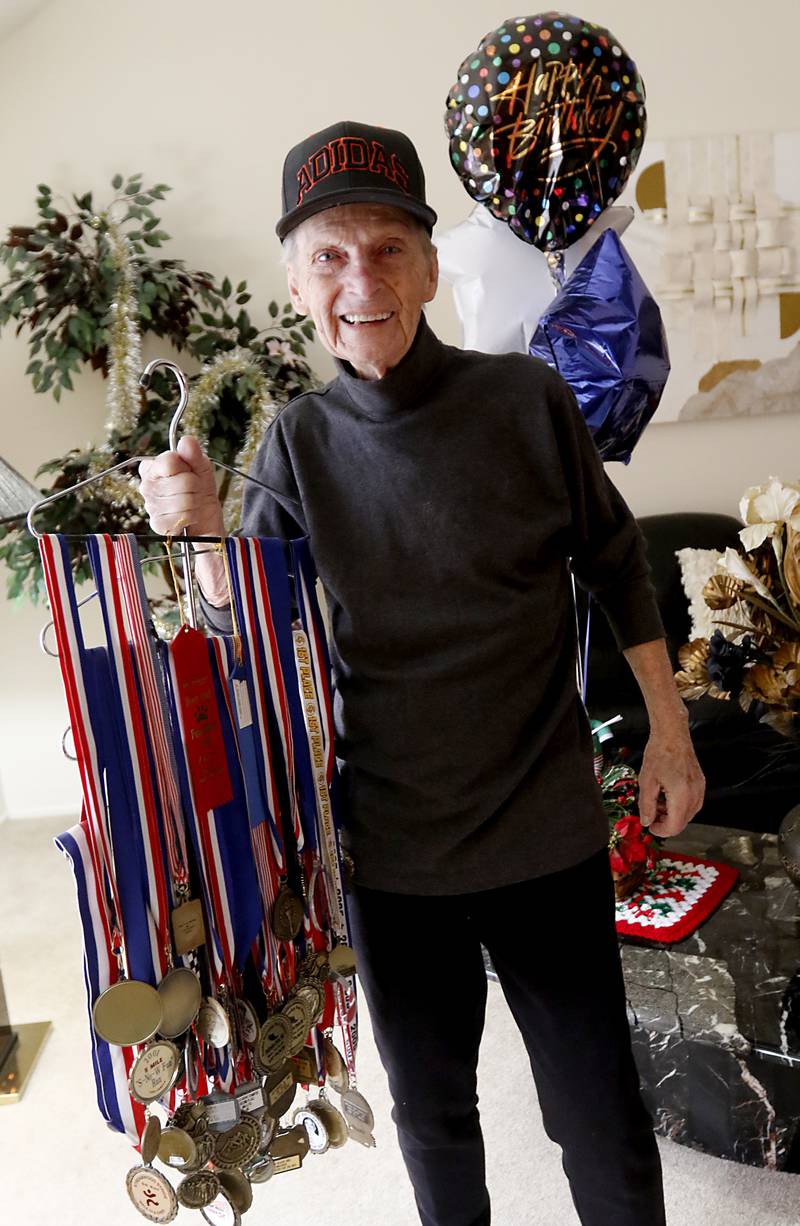 George Diedrichs, a local runner who just celebrated his 90h birthday, holds some of his running medals at his home in Crystal Lake on Thursday, Jan. 5, 2023.