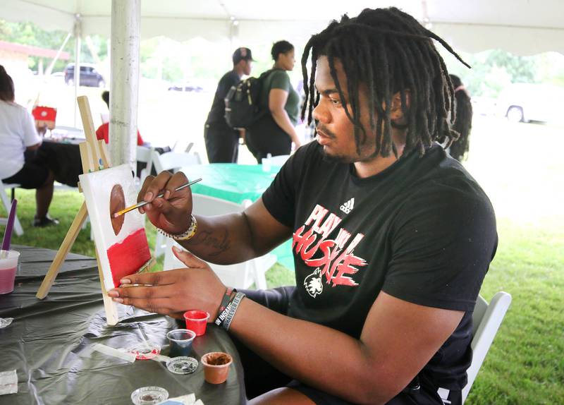 Abiathar Curry, a football player at Northern Illinois University, works on a painting in the art area during the Juneteenth Community Celebration Saturday, June 15, 2024, at Hopkins Park in DeKalb.