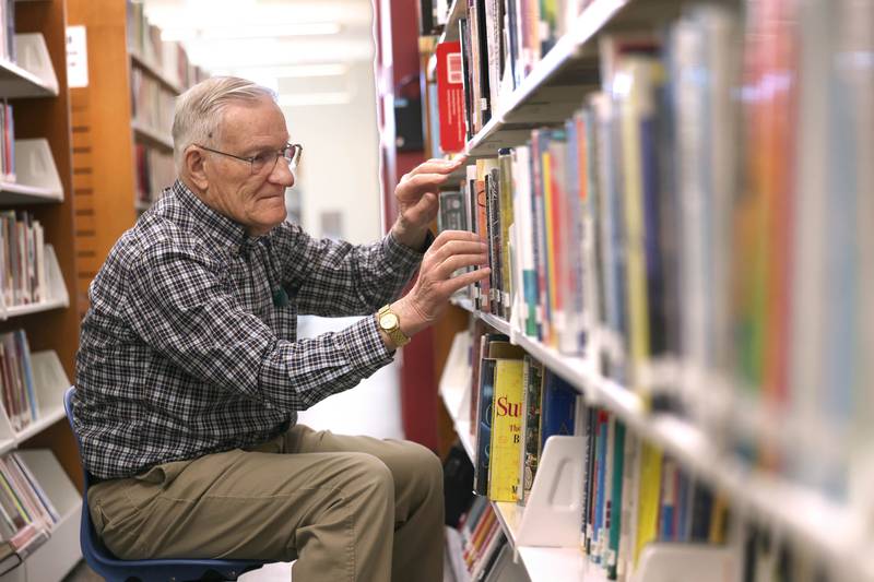 Longtime DeKalb Public Library volunteer Paul Mandigo, 83, straightens up books on the shelves Wednesday, March 25, 2026, at the library in DeKalb.